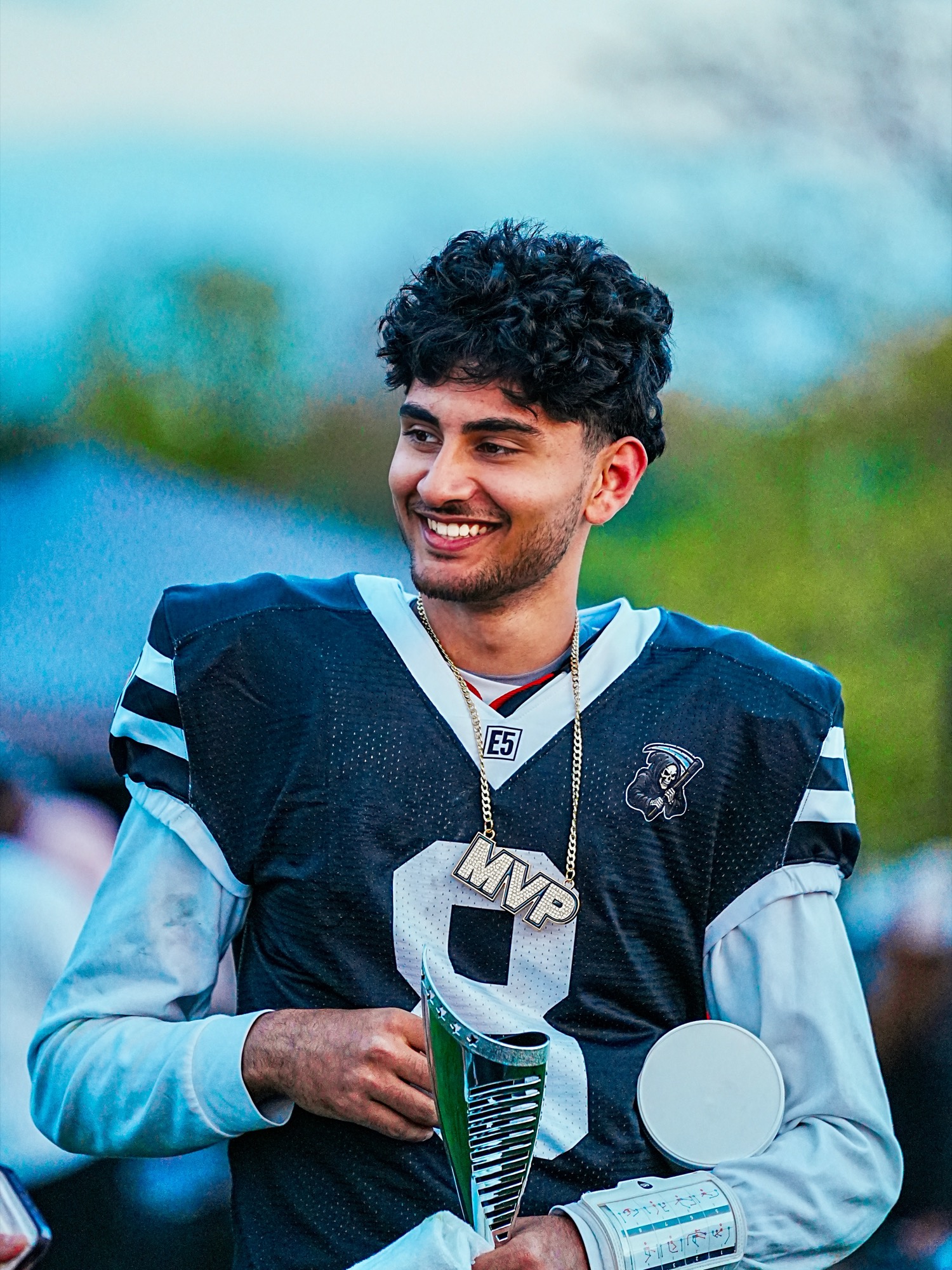 Adam Hydari with his MVP trophy in American football uniform